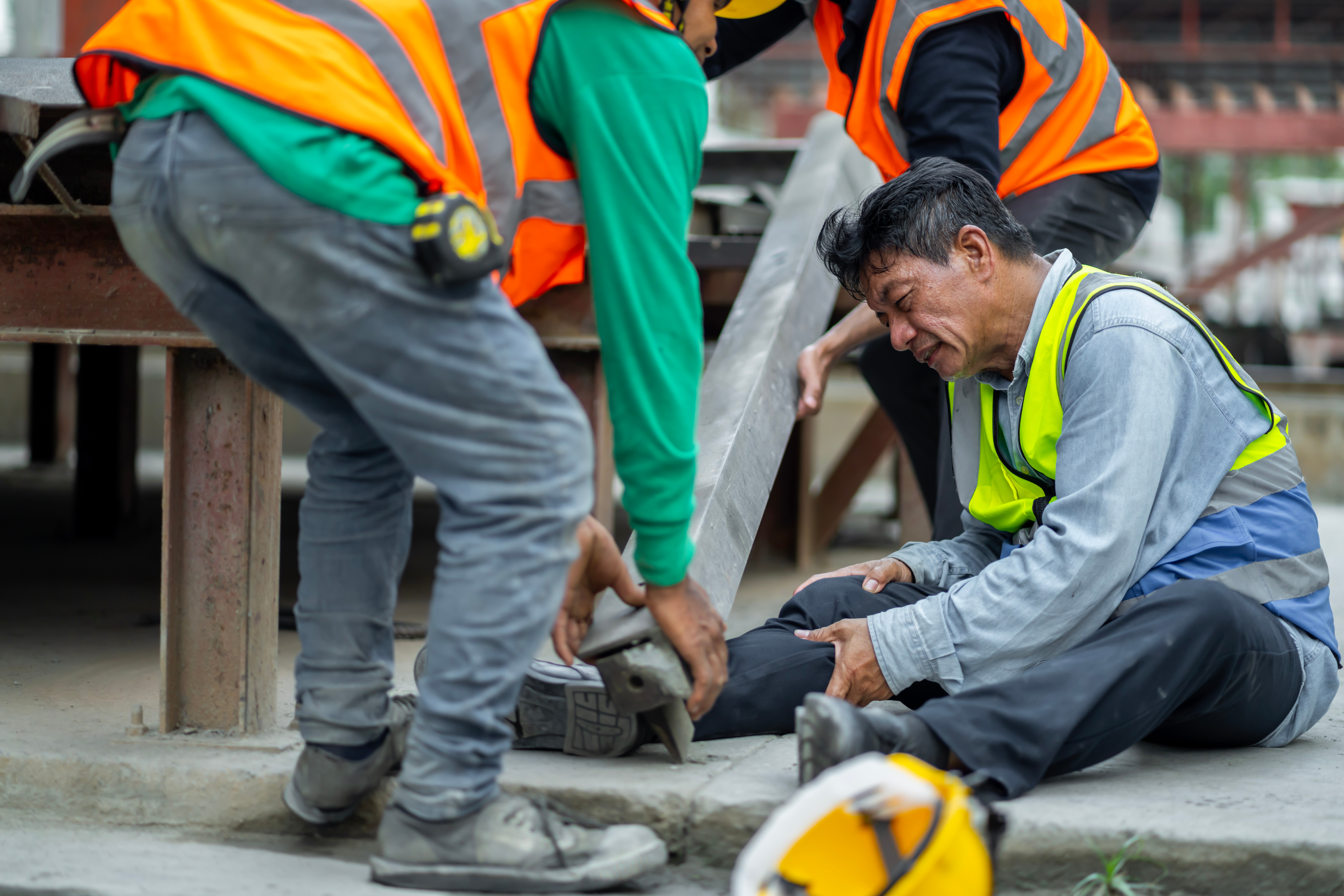 engineer has an accident where steel falls on his leg at work, causing serious leg injuries. and get help from colleagues in the area under construction industrial factory, concept, safe work