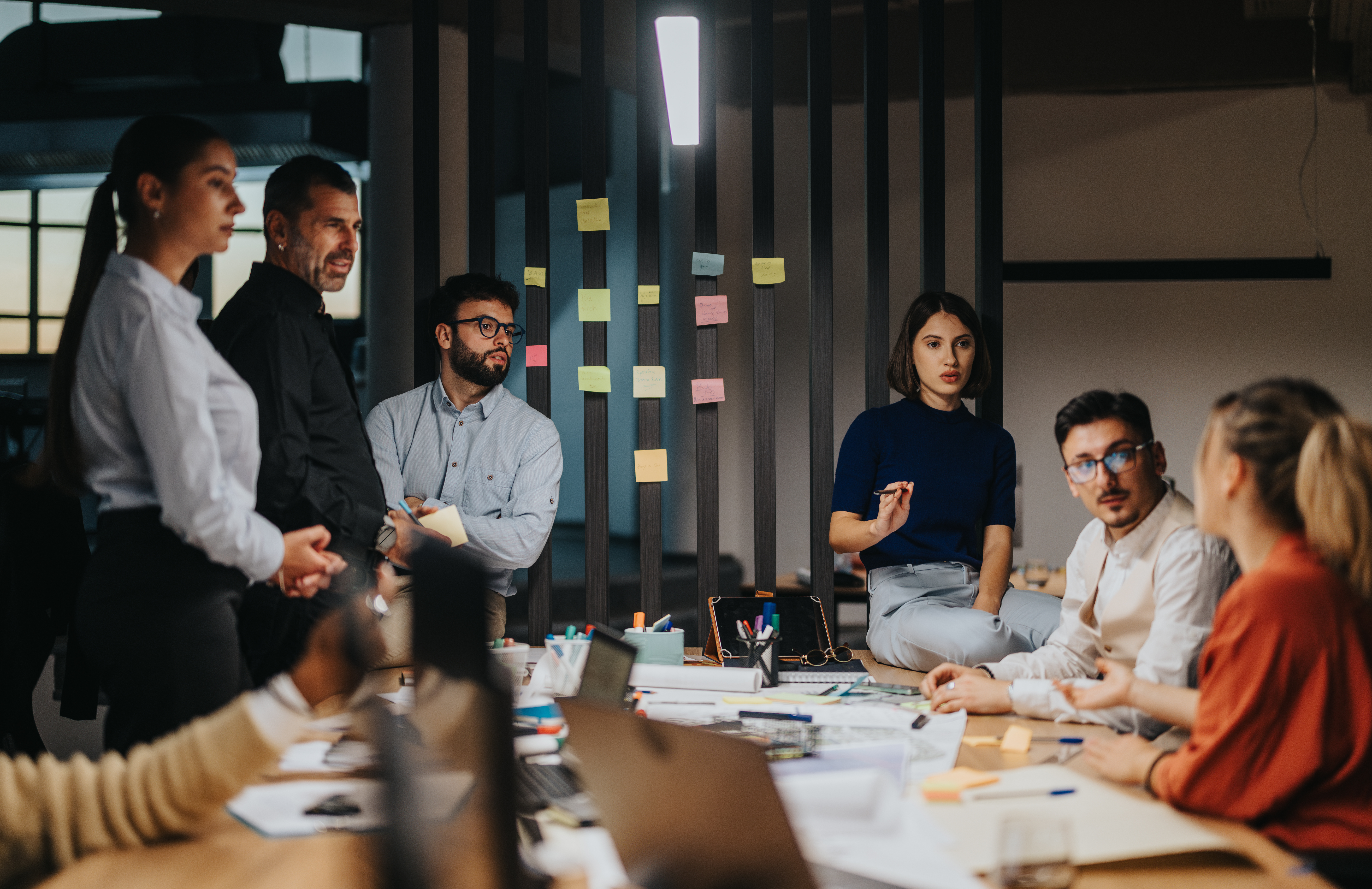 Diverse professionals discussing ideas and projects during a workplace meeting. The atmosphere is dynamic and collaborative, with various people contributing to the conversation in a modern office setting.