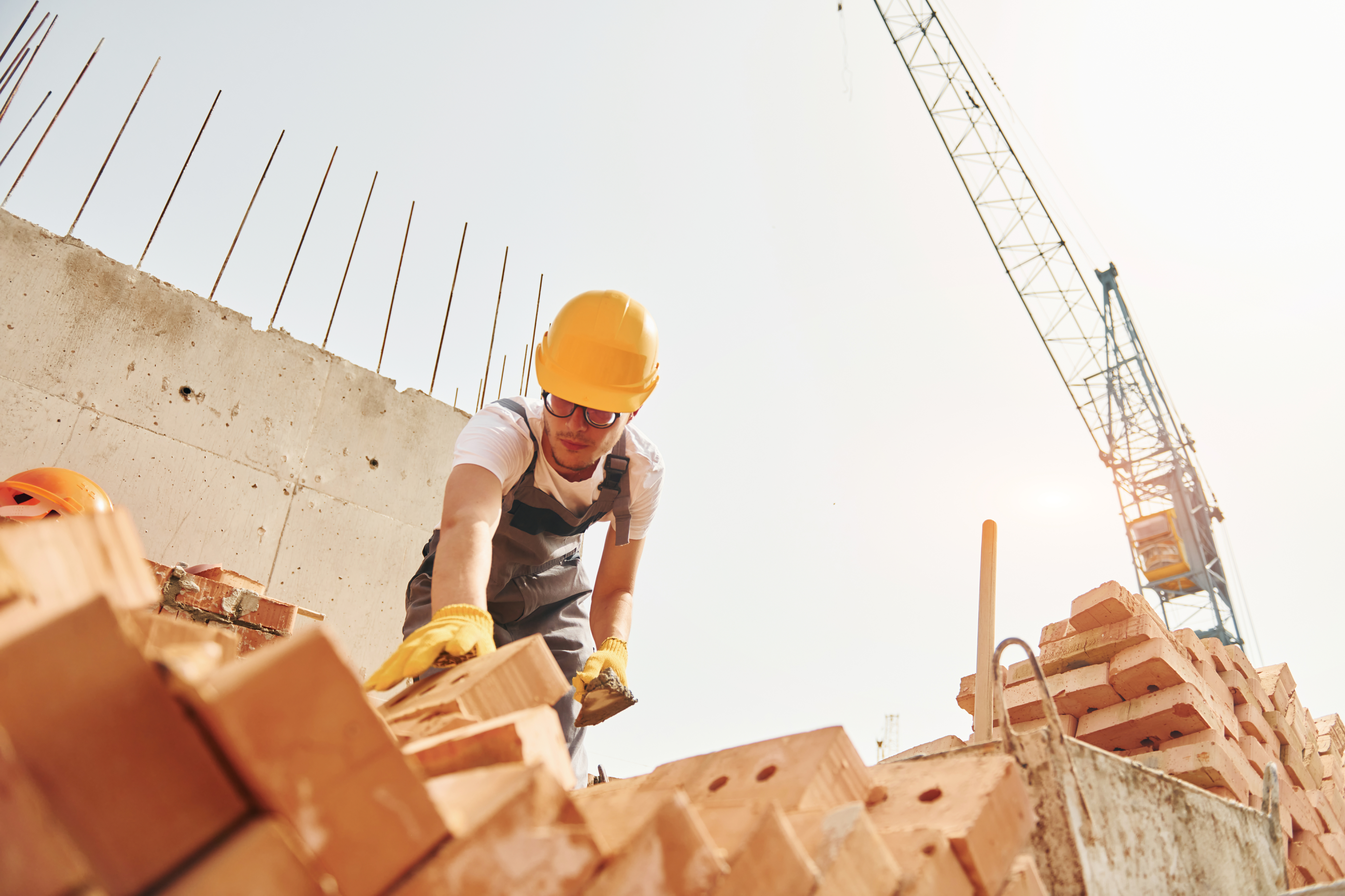 Using bricks. Young construction worker in uniform is busy at the unfinished building.